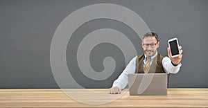 Man sitting in front of laptop and showing smartphone to camera