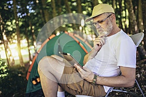 Man sitting in front of a tent and using digital tablet