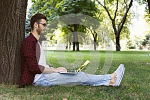 Man sitting on grass with laptop outdoors