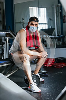 Man sitting in the gym with a towel around his neck. Surrounded by machines and weights. Health and wellness concept