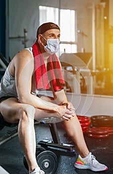 Man sitting in the gym with a towel around his neck. Surrounded by machines and weights. Health and wellness concept