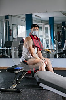 Man sitting in the gym with a towel around his neck. Surrounded by machines and weights. Health and wellness concept