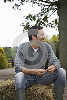 Man Sitting On Haybale Outdoors