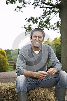 Man Sitting On Haybale Outdoors