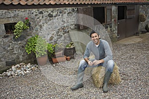 Man Sitting On Haybale Outside Stable