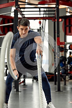 Man sitting on his toes holding a pair of battle ropes for workout. guy at the gym working out with fitness rope.