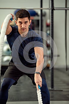 Man sitting on his toes holding a pair of battle ropes for workout. guy at the gym working out with fitness rope.