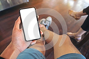 A man sitting and holding black mobile phone with blank white screen