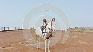 man sitting on horse for riding with white horse in an open field with a clear sky and desert in the background
