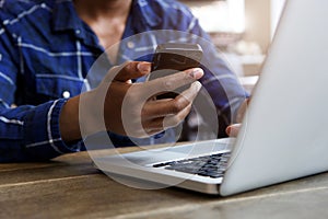 Man sitting indoors holding mobile phone with laptop