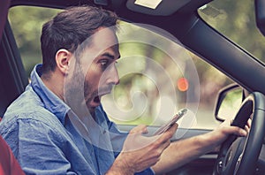 Man sitting inside car with mobile phone texting while driving