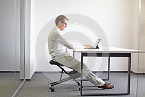 Man sitting on kneeling stool and working with tablet in his office