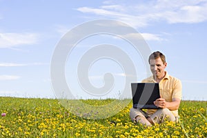 Man sitting with laptop computer in a meadow