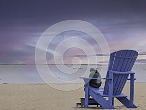 Man sitting on large adirondack chair on beach