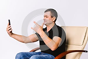 A man sitting in a leather armchair communicates non-verbally via video communication, showing I Love You to his photo