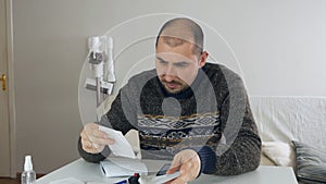 Man sitting in living room doing financial analysis, holding sales receipt, pile of receipts, worried about money