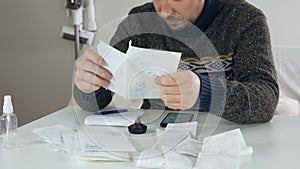 Man sitting in living room doing financial analysis, holding sales receipt, pile of receipts, worried about money