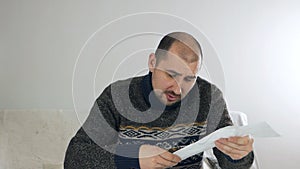 Man sitting in living room doing financial analysis, holding sales receipt, pile of receipts, worried about money