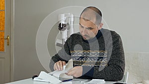 Man sitting in living room doing financial analysis, holding sales receipt, pile of receipts, worried about money