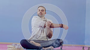 Man sitting in lotus pose on floor in studio and stretching arms