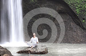 Man sitting in meditation yoga on rock at waterfall Tibumana photo
