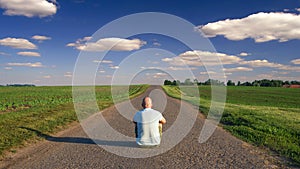 Man sitting in the middle of the country road on sunny summer