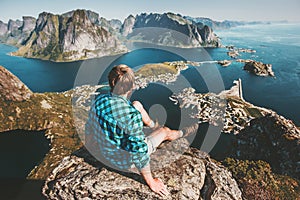 Man sitting on mountain top cliff above sea and rocks