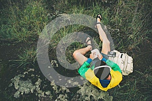 Man sitting in nature with backpack, photo camera, listening music and writing in the notebook, top view