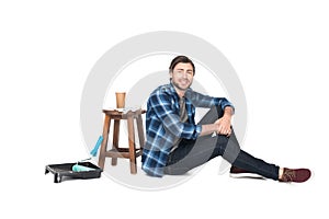 man sitting near chair with coffee cup and roller tray with paint roller