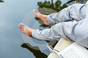 A man sitting near the water. Foots over the water. Relaxing concept