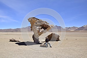 A man is sitting next to the famous stone tree rock formation (Arbol de Piedra) in the Siloli desert. Bolivia