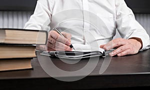 Man sitting at office desk with books or codes and taking notes in diary. Man hands closeup. Planning or information