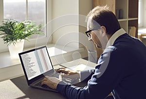 Man sitting at office desk and working with business documents and spreadsheets on laptop