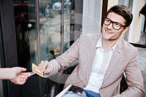 Man sitting in outdoor cafe and paying by credit card