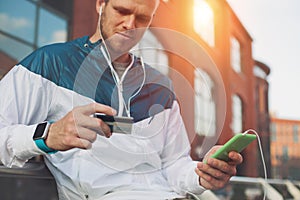 Man sitting outdoors with credit card and mobile phone, internet banking and web payment