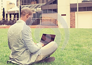 Man sitting outside corporate office working on laptop computer
