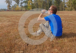 A man  sitting in a park is drinking