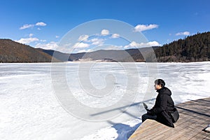 A man sitting at Potatso National Park or Pudacuo National Park during winter with mountain and frozen lake scenery with snow cove