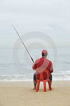 Man Sitting On Red Plastic Chair And Fishing At Beach