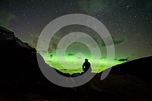 Man sitting on a rock in the mountains watching the Northern Lights