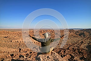 Man Sitting on the Rock Raising Arms Appreciating the Awesome view of the Moon Valley or Valle de la Luna