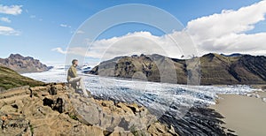 Man sitting on rocks overlooking Skaftafellsjokull part of Vatnajokull glacier in Skaftafell national park, Iceland