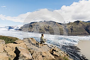 Man sitting on rocks overlooking Skaftafellsjokull part of Vatnajokull glacier in Skaftafell national park, Iceland