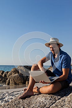 Man sitting on the rocks and using laptop on beach