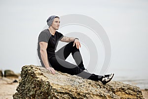 Man sitting on rocky beach in the sunset at the sea.