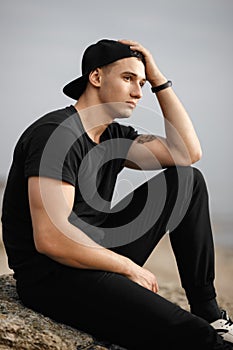 Man sitting on rocky beach in the sunset at the sea.