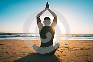 Man sitting on the sand and practise yoga or meditates on the beach with ocean view at sunset or sunrise