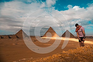 Man sitting on the sandy desert dunes posing in front of the great pyramids of giza. Traveling egypt in winter time, tourists