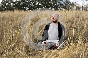 man sitting and smiling on the grass with a laptop