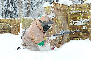 Man sitting on snow behind wooden fortification playing paintball